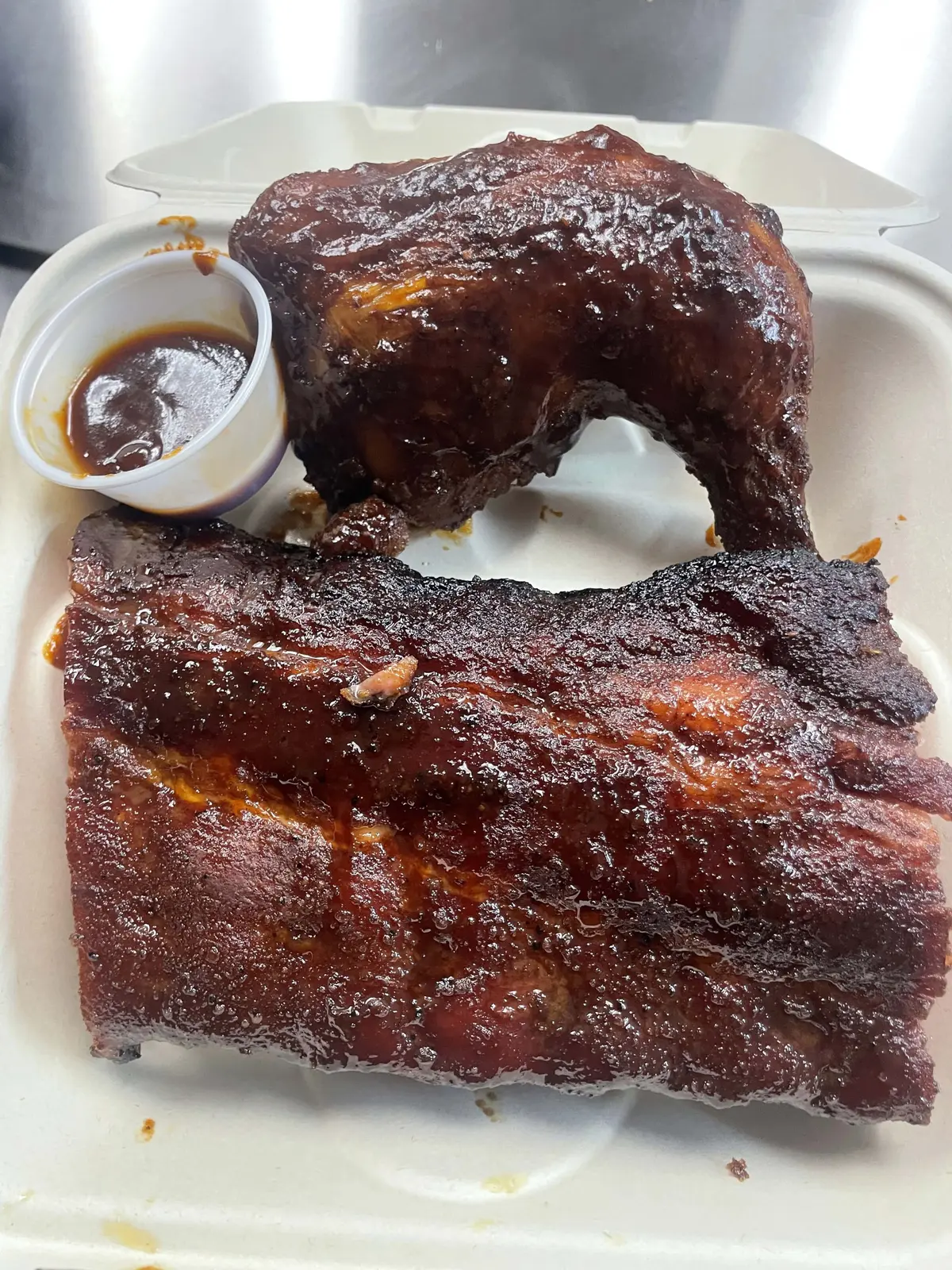 A to-go plate of glazed ribs and a smoked chicken quarter with sauce
